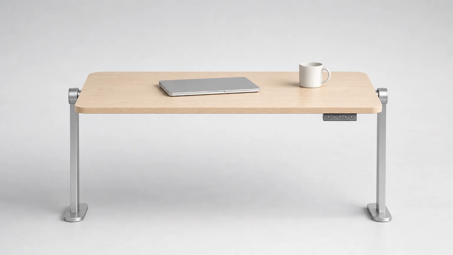 Versoflip One standing desk seen from the front: a single pale ash desktop held level between two round steel pivot hubs on slim silver columns, nothing beneath it, with a laptop, a mug and the keypad under the front edge